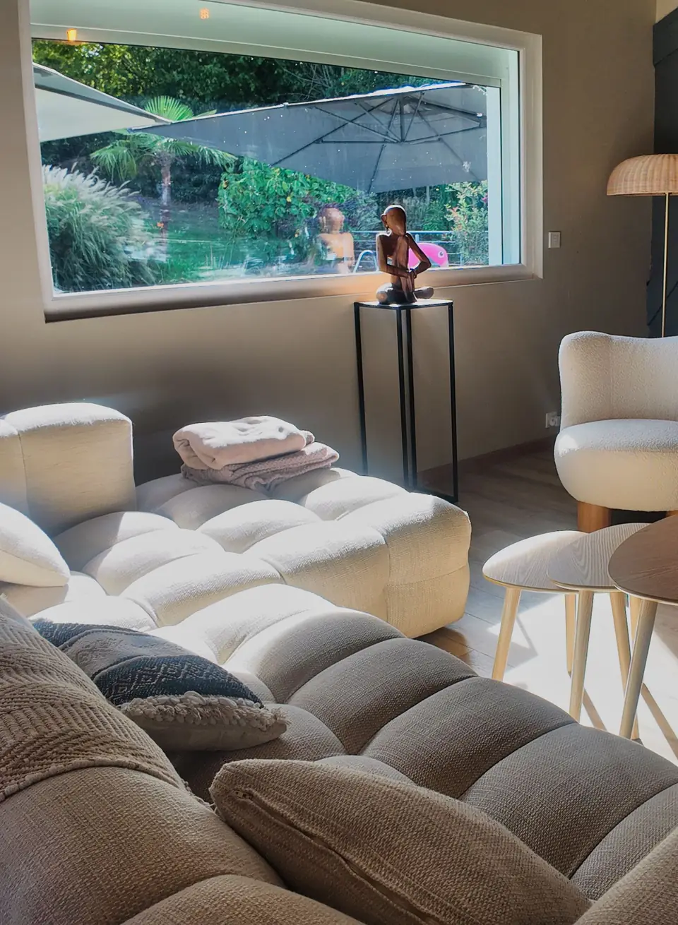Le salon du Chalet Normand : le grand canapé clair, un fauteuil et la baie qui donne sur la piscine