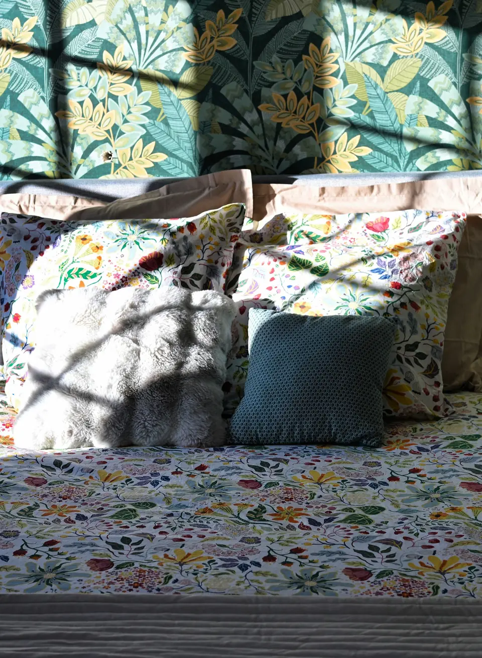 Une chambre du Chalet Normand : le lit au couvre-lit fleuri devant un papier peint de feuillages, dans un rayon de soleil