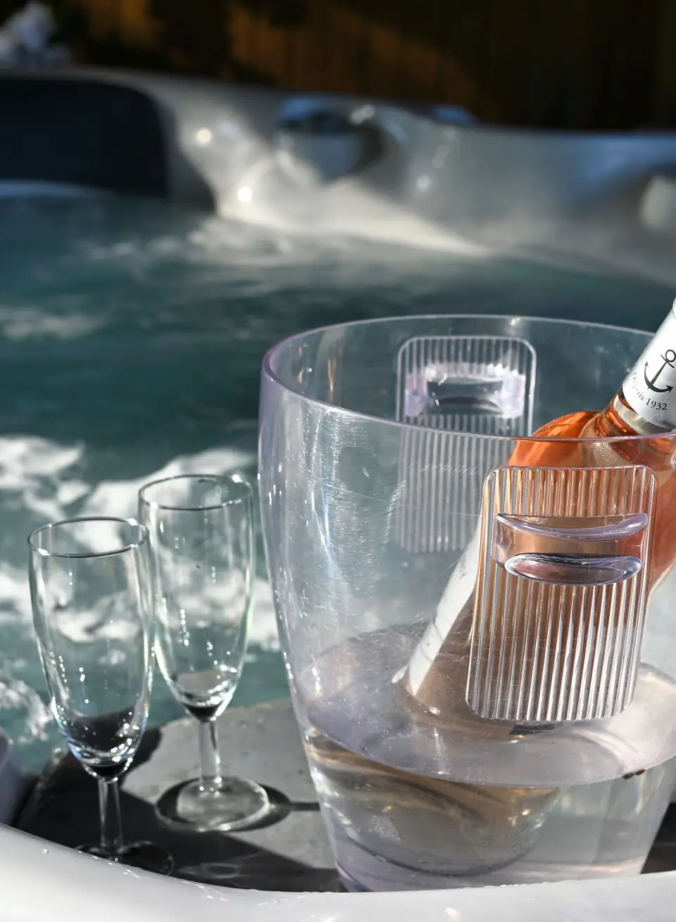Deux flûtes et une bouteille de rosé dans un seau, au bord du jacuzzi